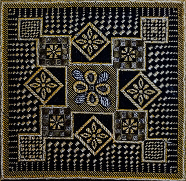 Geometric gold and silver thread embroidery pattern with floral star motifs on dark black fabric background.
