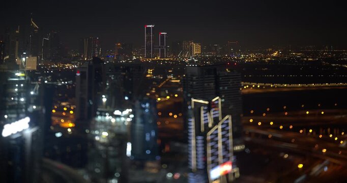Dubai skyline at night, One Zabeel twin towers stand on the horizon, lit office towers and highway lights fill the frame, tilt shift lens blurs the city into a miniature model, timelapse