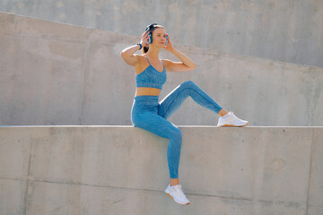 Fototapeta premium Sporty woman enjoying music while stretching outdoors at modern concrete structure