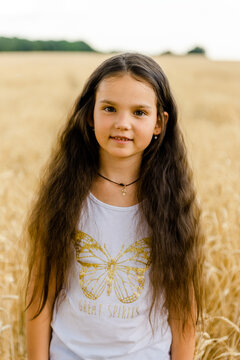 Happy little girl standing with arms open in golden wheat field under blue sky