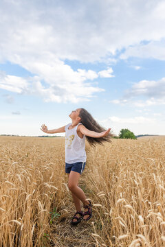 Happy little girl standing with arms open in golden wheat field under blue sky