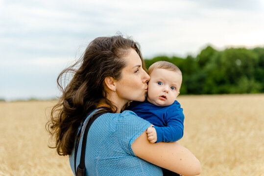 A young woman with her little son stands in a wheat field in the summer. Harmonious parenting of children.
