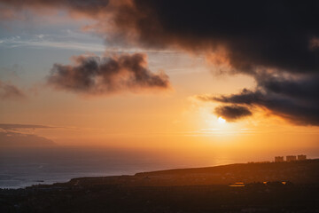 Fototapeta premium Dramatic sunset over the ocean with clouds and coastal town in Tenerife
