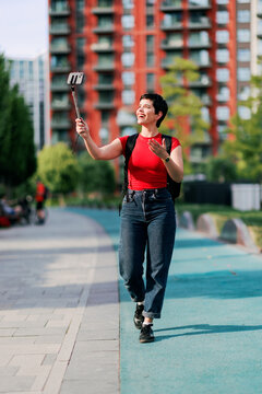 Woman vlogging with smartphone on selfie stick in city