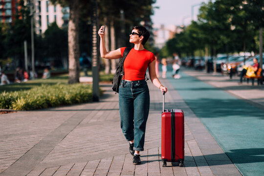Young woman traveling pulling red suitcase recording video