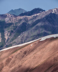 Diagonal snow cornice crossing rugged brown and green mountain slopes, highlighting contrasting textures of the alpine landscape in western Tien Shan, Uzbekistan. © Kolchanov