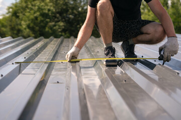 The builder measures the width of the corrugated sheet on the roof with a tape measure © Sergey