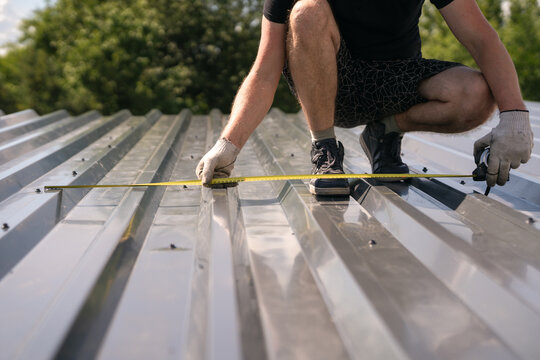 The builder measures the width of the corrugated sheet on the roof with a tape measure