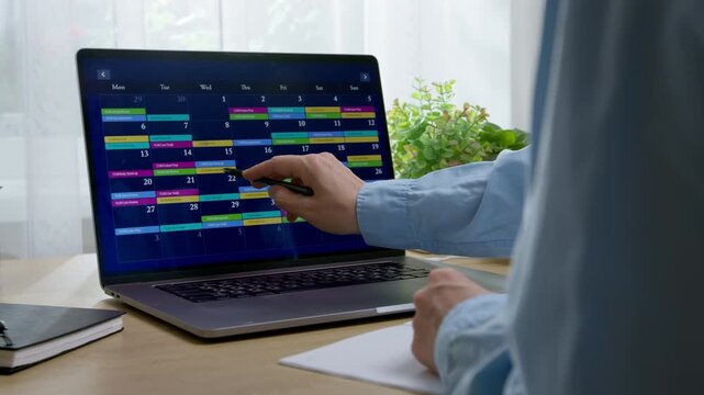Close-up of person pointing at online planner and calendar app on modern laptop display. Time management, task planning, and business organization concept in bright workspace.