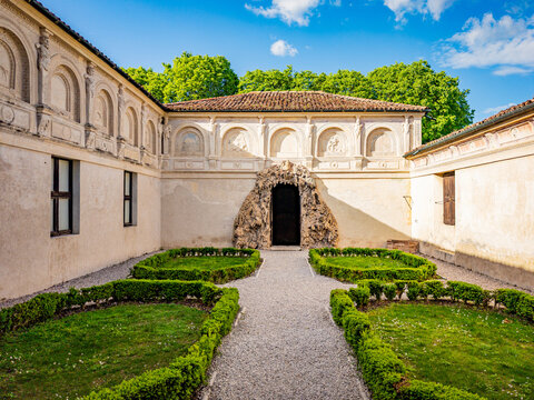 Palazzo Te's secret garden featuring a rustic grotto entrance and Renaissance architecture with classical reliefs, creating a tranquil historical atmosphere under a clear sky