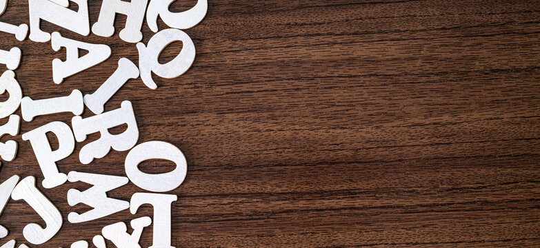 Few scattered white wooden letter tiles on empty dark brown wooden background, minimalist typography concept
