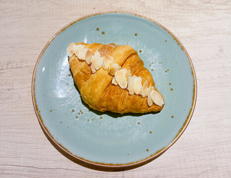 Golden Almond Croissant Served on a Blue Ceramic Plate with Wooden Table Background