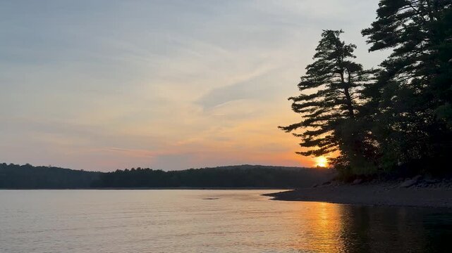Sunset Over Calm Lake with Pine Trees and Water Reflection