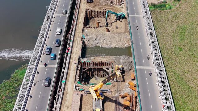 Excavator building bridge piers in a waterway beside an elevated vehicle bridge