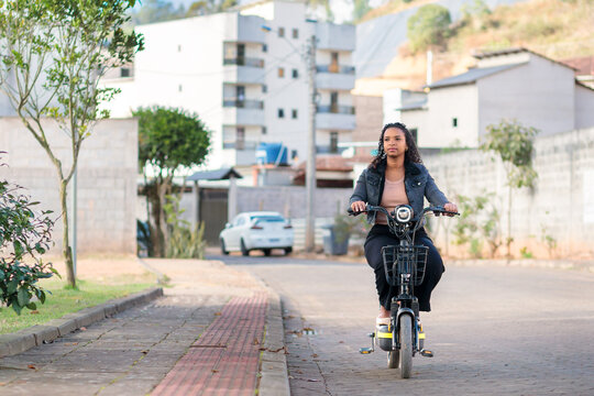 Young Black Brazilian woman commuting on an electric bicycle in a residential neighborhood, representing sustainable mobility, eco-friendly transportation, and modern daily urban life.
