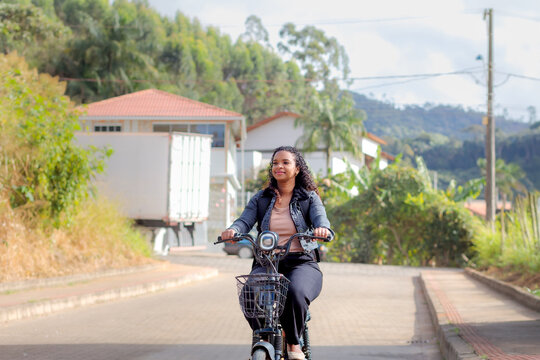Young Black Brazilian woman commuting on an electric bicycle in a residential neighborhood, representing sustainable mobility, eco-friendly transportation, and modern daily urban life.
