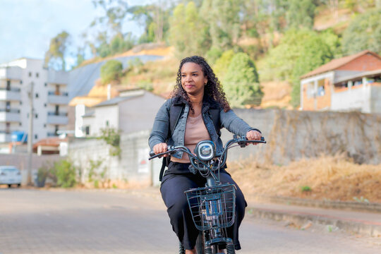 Young Black Brazilian woman commuting on an electric bicycle in a residential neighborhood, representing sustainable mobility, eco-friendly transportation, and modern daily urban life.