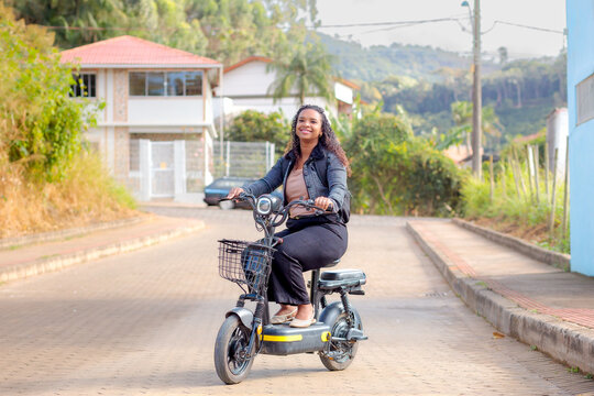 Young Black Brazilian woman commuting on an electric bicycle in a residential neighborhood, representing sustainable mobility, eco-friendly transportation, and modern daily urban life.