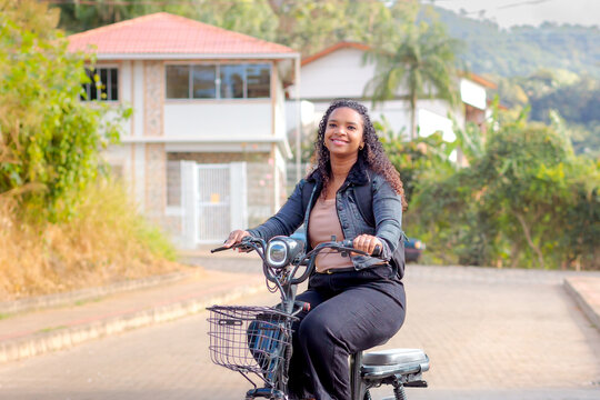 Young Black Brazilian woman commuting on an electric bicycle in a residential neighborhood, representing sustainable mobility, eco-friendly transportation, and modern daily urban life.