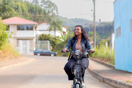 Young Black Brazilian woman commuting on an electric bicycle in a residential neighborhood, representing sustainable mobility, eco-friendly transportation, and modern daily urban life.