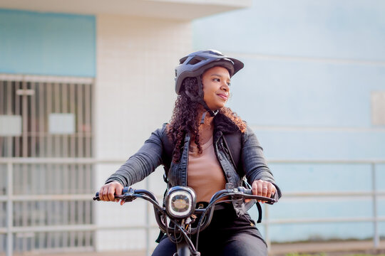 Young Black Brazilian woman commuting on an electric bicycle with a helmet, representing modern urban mobility, daily transportation, and sustainable mobility.