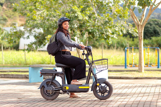 Young Black woman with helmet and backpack riding her electric bicycle, representing safe and sustainable daily urban commuting.