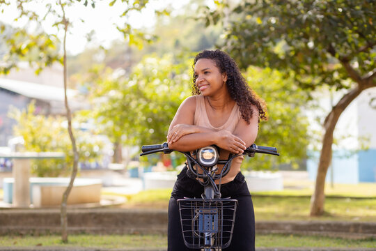 Young Black Brazilian woman enjoying a break with her electric bicycle, representing urban mobility, everyday commuting, and sustainable transportation.