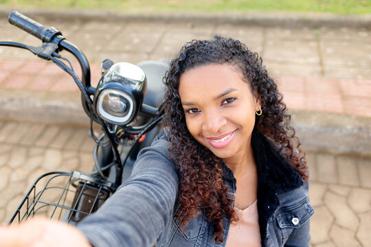 Young Black woman smiling and taking a selfie on her electric bicycle outdoors, representing sustainable urban mobility and youthful independence.
