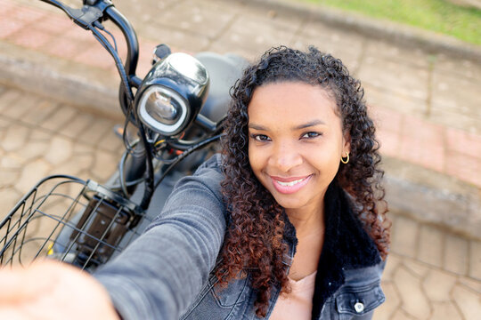 Young Black woman smiling and taking a selfie on her electric bicycle outdoors, representing sustainable urban mobility and youthful independence.