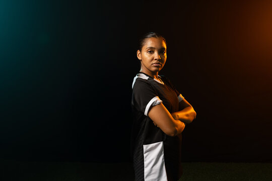 African American woman posing with crossed arms in studio on turf wearing black jersey, copy space