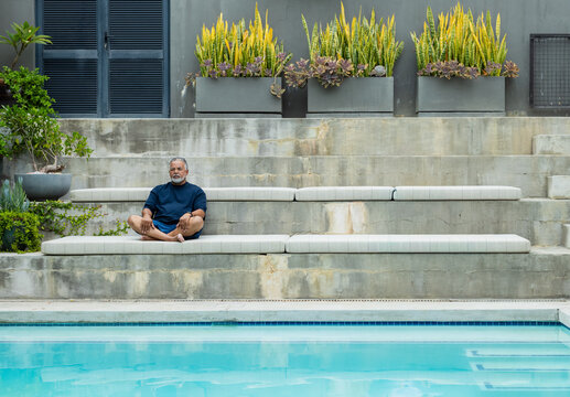 Senior African American man sitting cross-legged on tiered bench by pool in navy shirt, copy space