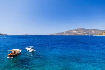 Two small boats tethered on a vibrant blue sea with clear skies and distant island hills, evoking summer travel and peaceful coastal scenery ideal for vacation, leisure and nautical themes. Turkey © evannovostro