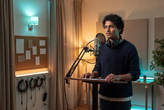 Young man recording voiceover at standing desk with condenser microphone in home studio