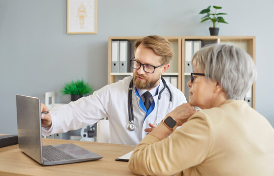 Doctor or nurse conducts consultation for elderly senior patient in hospital using laptop, providing advice and aid in a professional setting with focus on healthcare and care daily.