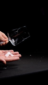 Person's hands holding a shattered wine glass and catching falling glass shards, illustrating concepts of damage, fragility, and unexpected accidents against a dark background