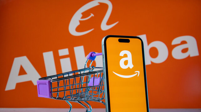 Small shopping cart and smartphone displaying amazon logo with alibaba branding in blurred background.