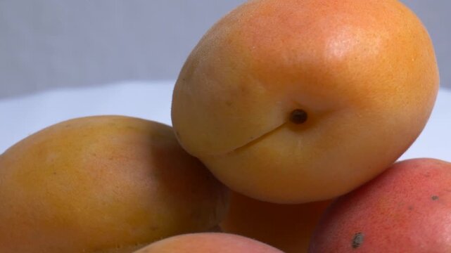 Close-up of fresh orange apricots rotating on a white plate, showcasing their soft fuzzy skin and vibrant summer color under studio lighting.