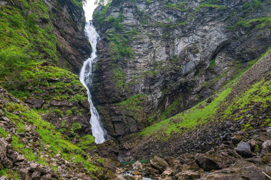 Tall narrow waterfall flowing through a rocky green ravine in the Geiranger region, Norway.
