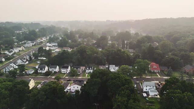 Panoramic aerial view of a Connecticut suburb covered in wildfire smoke haze, showing homes, roads, and trees under poor air quality, highlighting climate change, pollution, and environmental impact.