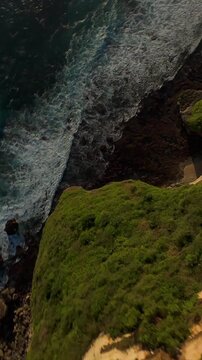 Vertical video. Extreme FPV Drone Dive Down Karang Boma Cliff Toward Powerful Ocean Waves, First Person Descent Above Rocky Shoreline And Hidden Cove, Adrenaline And Freedom