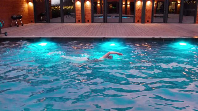 Open air pool video of woman training front crawl in evening light. Dynamic sports scene highlights crawl technique, stamina, splash detail, and elegant residential setting