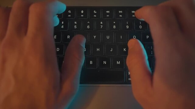 Close up on hands typing on laptop keyboard in dark office desk at night. Person writing programming or coding using portable computer. Hacker or writer rapidly pressing on keys and buttons. Top shot