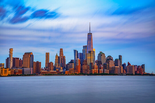Long-exposure view of New York City showing Lower Manhattan and the Financial District at sunset, with One World Trade Center towering across the Hudson River from New Jersey.
