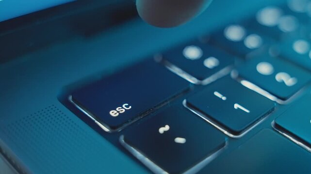 Extreme close up on finger pressing on Escape or Esc key on laptop keyboard. Dark office desk or house room. Person or hacker clicking on key to exit or finish a task. Leaving app or closing window