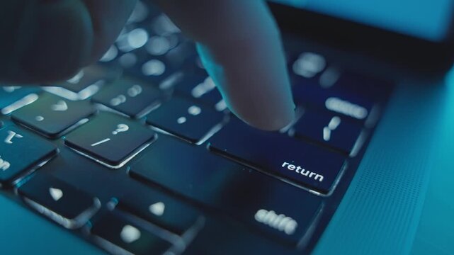 Close up on finger clicking various times on Return key on laptop keyboard. Person using computer at night in dark office presses to enter or initiate task or command on software application