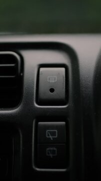 Close-up of a finger turning off the rear window defroster button on a car dashboard. Vehicle interior scene. Climate control, driving safety, and convenience.