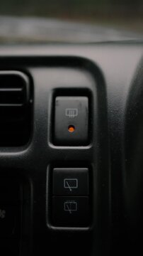 Close-up of a finger turning on the rear window defroster button on a car dashboard. Vehicle interior scene representing climate control, driving safety, and convenience.