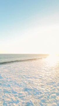 Vertical video. Drone Flying Into Bright Sunset Above Nyang Nyang Beach, Golden Ocean Surface And Gentle Breaking Waves Creating A Dreamlike Tropical Scene
