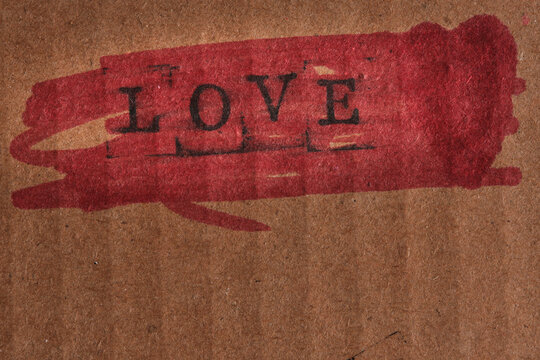 Word LOVE stamped over bright red painted brush stroke on textured brown cardboard paper.