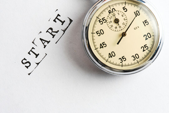 Vintage mechanical stopwatch with word START stamped in black letters on white background paper.